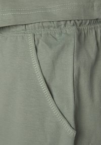 Light green cotton fabric with elastic waistband and side pocket. Visible stitching detail enhances structure and texture.