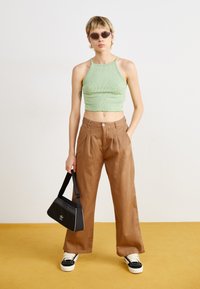 Lysegrønn ribbet crop topp, brune vide bukser, svart veske med logo, svart og hvite sneakers, og solbriller. Rent design, uformell stil.