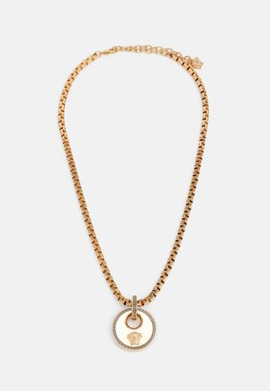 Gold metal chain necklace with a large circular pendant featuring intricate black detailing and a lion motif. The chain has a flat link design.