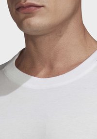 Bílý bavlněný tričko s kulatým výstřihem. Textura vypadá hladce, což ukazuje na přiléhavý a čistý design s minimálním šitím.