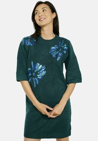 Teal gebreid jurkje met korte mouwen, voorzien van blauwe pailletten bloemmotieven. Zachte textuur, rechte snit en knielange ontwerp.