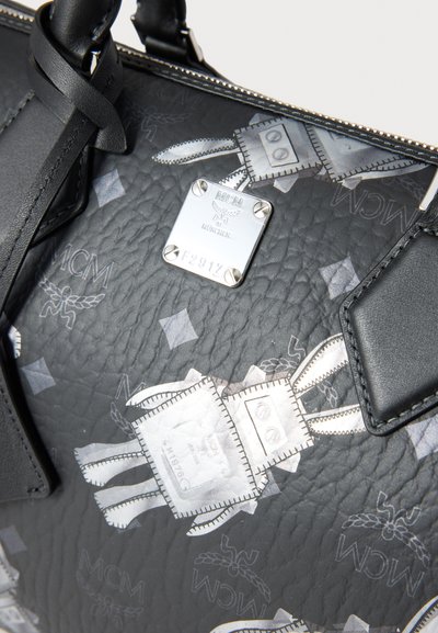 Fekete texturált bőr táska, melyen fém logó tábla, részletes ezüst minták játékos motívumokkal, valamint fekete bőr díszítések találhatók.