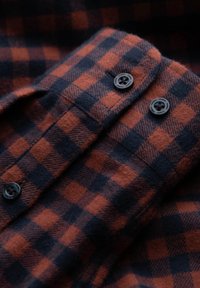 Camicia in flanella a quadri rossi e blu navy con una texture liscia, caratterizzata da bottoni in plastica nera e colletto ripiegato.