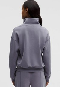 Violetti poolopaita, jossa on korkea kaulus, pehmeä kangas, alaspäin lasketut olkapäät sekä ribbineulokset hihansuissa ja helmassa. Ei näkyviä logoja tai kuvioita.