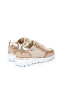Zapatillas de cuero beige con detalles en dorado, que cuentan con un cierre de cremallera, detalles de tachuelas en los laterales y una suela gruesa blanca.
