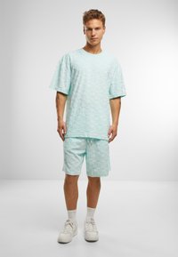 Mintgrøn tekstureret t-shirt med korte ærmer og matchende shorts. Begge har et hævet mønster. Afsluttet med hvide sneakers.
