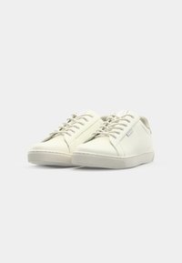 Baskets blanches en cuir avec une texture lisse, présentant des bouts ronds, un système de laçage et une semelle en caoutchouc. Les accents comprennent des détails de couture subtils.