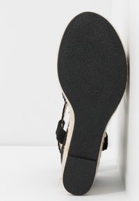 Semelle en caoutchouc noir d'une sandale pour femme avec un motif texturé, une semelle intérieure en jute style espadrille visible et des brides tressées noires.