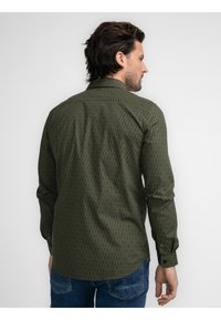 Camisa verde con patrón, de manga larga, con cuello clásico y puños de botón. Presenta un diseño geométrico con una textura sutil.