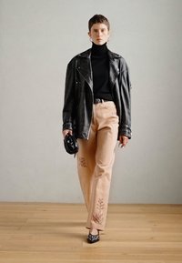 Μαύρο δερμάτινο μπουφάν μηχανής, εφαρμοστό μαύρο ζιβάγκο, ανοιχτό μπεζ παντελόνι με λουλουδάτη κεντημένη διακόσμηση, μαύρες ανοιχτές παντόφλες και μαύρη τσάντα χειρός.