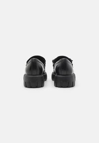 Zwarte leren schoenen met een ronde neus en een dikke rubberen zool, met een gekartelde hak en decoratieve stiksels op het bovenwerk.