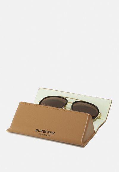 Brun lærsolbrilleetui med preget "BURBERRY"-tekst, som inneholder mørke linser rammet i gulltone metall, med en lyse farget innside.
