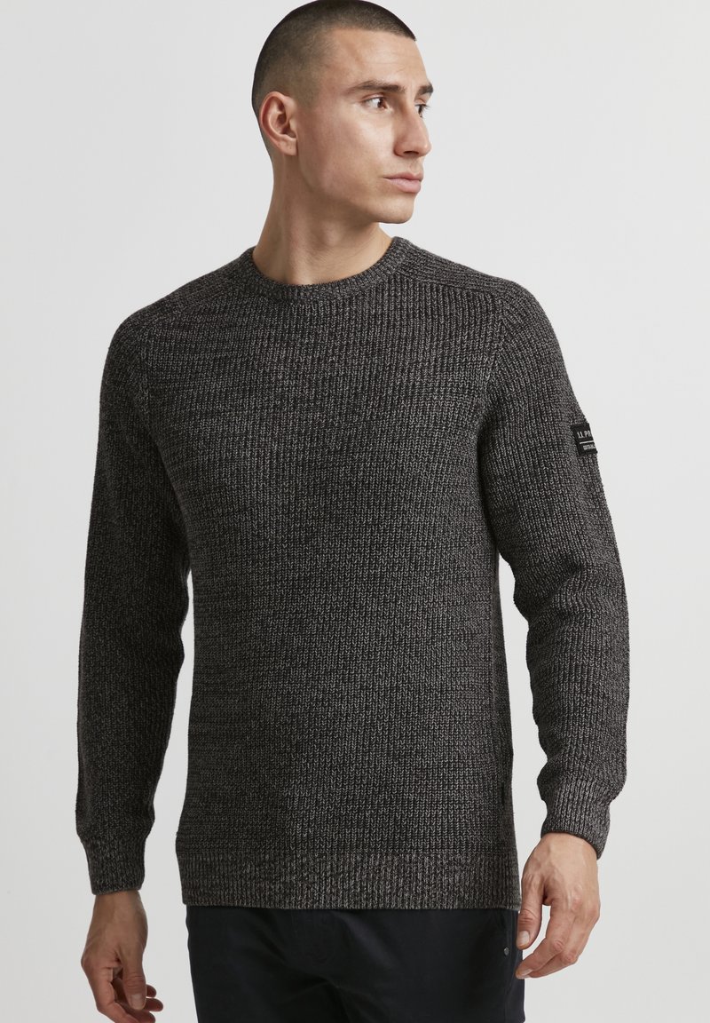 Dark gray knitted sweater with a crew neckline, textured fabric, ribbed cuffs, and a brand tag on the left sleeve.