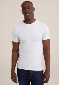 Witte katoenen t-shirt met korte mouwen, ronde halslijn en een slim fit. Draagt met blauwe denim jeans, weergegeven tegen een neutrale achtergrond.