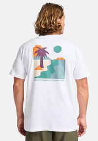 Fehér pamut póló, hátán színes grafikával, amelyen pálmafák, nap, felhők és víz látható, feliratozva: "BILLABONG ADVENTURE DIVISION."
