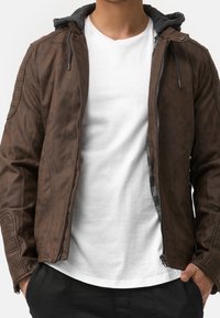 Brown leather jacket with gray hood, zipper closure, and stitched shoulder details. Worn over a white t-shirt.