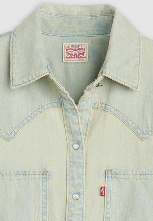 Jasnoniebieska koszula jeansowa z klasycznym kołnierzem, zatrzaskami na przodzie, kieszenią na piersi oraz metką w czerwono-białym wzorze. Charakteryzuje się wyblakłą fakturą.