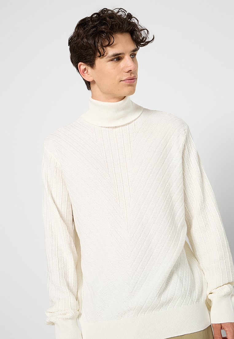 Maglione bianco a collo alto in maglia con un motivo a zig-zag testurizzato e polsini a costine. La vestibilità morbida e il tessuto soffice creano una silhouette confortevole.