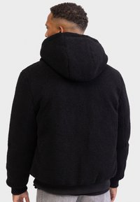 Black fleece jacket with a hood, featuring a textured, fluffy surface. It has ribbed cuffs and a hem, designed for a relaxed fit.
