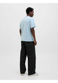 Light blue short-sleeve T-shirt paired with loose-fitting dark denim jeans. Textured fabric, relaxed fit, and visible stitching details.