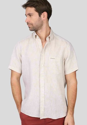 Chemise beige à manches courtes avec un motif texturé subtil, col boutonné, poche poitrine et boutons blancs.