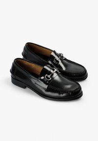 Mocasines de cuero negro con punta redondeada, herrajes decorativos con hebilla, acentos cosidos y un tacón bajo y sólido. Acabado brillante y suave.