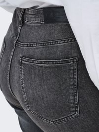 Close-up van een persoon die een donkergrijze spijkerbroek draagt met een achterzak en een zwart leren merklabel op de tailleband.