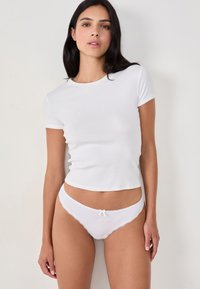T-shirt bianco in cotone con maniche corte abbinato a uno slip di pizzo bianco con un piccolo fiocco e dettagli ricamati sulla parte frontale.