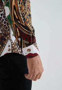 Chemise à manches longues imprimée avec un mélange de motifs animaliers et floraux. Présente des accents dorés et des poignets à boutons. Tissu : lisse, léger.