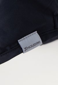 Navy fabric patch with grey stitching, featuring a rectangular tag embossed with "HOUDINI" in black letters, displaying a smooth texture.