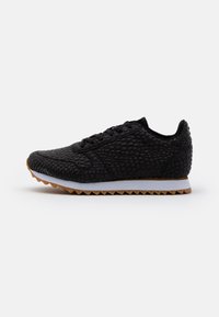 Black sneaker with textured upper resembling scales, lace-up design, and a white midsole. Outsole features a serrated pattern for traction.