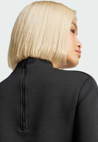 Svart zip-up sweatshirt med fokus på en hög halsringning och en synlig dragkedja på baksidan, tillverkad av ett slätt tyg med en mjuk textur.