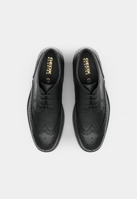 Brogues en cuir noir avec perforations décoratives, finition lisse et semelles plates. Comprend des lacets et un logo "GEOX RESPIRA" en doré.
