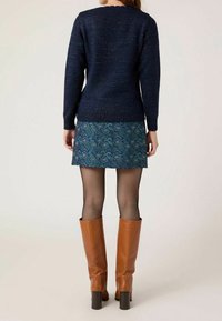 Marinblå stickad tröja med en strukturerad yta, tillsammans med en blå blommönstrad kjol, nätstrumpor och knähöga bruna läderstövlar.