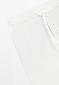 Gros plan sur la ceinture d'un pantalon en lin blanc avec bande élastique et cordon noué sur fond clair.