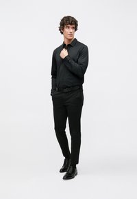 Zwart overhemd met lange mouwen en knoopsluiting, voorzien van een klassieke kraag, gecombineerd met zwarte slim-fit broek en zwarte leren veterschoenen.