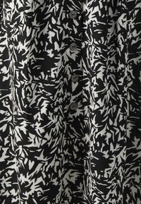 Mustekki ja valkoinen kuvioitu kangas, jossa on abstrakteja muotoja, ja edessä napit. Tekstuurin näyttää olevan sileä ja kevyt.