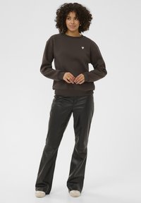 Hnědá mikina s malým bílým srdíčkovým logem, spárovaná s černými koženými kalhotami. Mikina má volný střih a žebrované manžety.