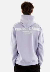 Felpa leggera color lavanda realizzata in tessuto morbido, con una grande stampa bianca sul retro: "PROJECT X PARIS MEMBERS' CLUB" con dettagli più piccoli.