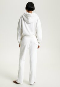 Sudadera blanca con un corte relajado y una gran capucha, combinada con pantalones de chándal blancos a juego. Tejido suave, diseño minimalista y sutiles detalles de costura.
