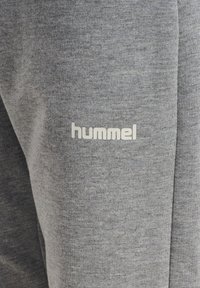 Zbliżenie na szary materiał z białym logo marki „hummel” nadrukowanym na teksturowanym materiale.