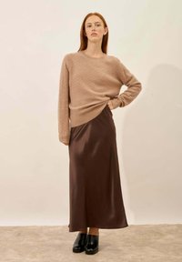 Beige gebreide trui met een ronde hals, gecombineerd met een bruine satijnen maxirok en zwarte plateauschoenen. Soepele texturen en eenvoudig ontwerp.