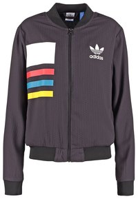 Giacca bomber nera con zip frontale, tessuto testurizzato, design a blocchi di colore con un rettangolo bianco e strisce rosse, blu e gialle.