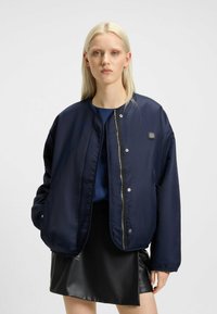 Navy blue bomber jacket made of smooth, lightweight fabric, featuring a front zip closure, snap buttons, and side pockets.