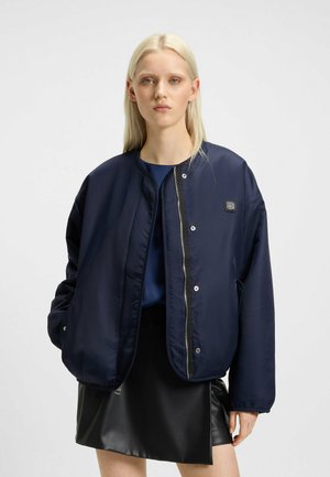 Navy blue bomber jacket made of smooth, lightweight fabric, featuring a front zip closure, snap buttons, and side pockets.