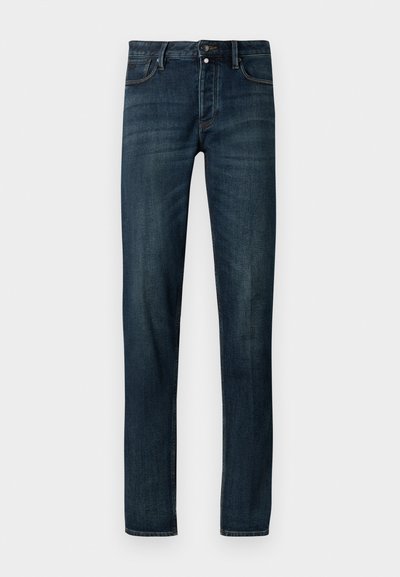 Jeans de ganga azul escura com um corte slim, apresentando um design de cinco bolsos, fecho com botão de metal e uma textura ligeiramente desbotada ao longo das pernas.