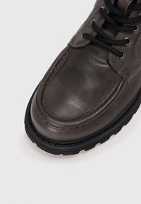 Botte en cuir gris au texture lisse, bout rond, œillets noirs et lacets, avec une épaisse semelle en caoutchouc noir.
