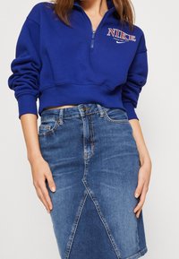 Mörkblå zip-up sweatshirt med hög krage och Nike-logotyp, tillsammans med en figurnära jeanspennkjol med diagonala sömdetaljer.