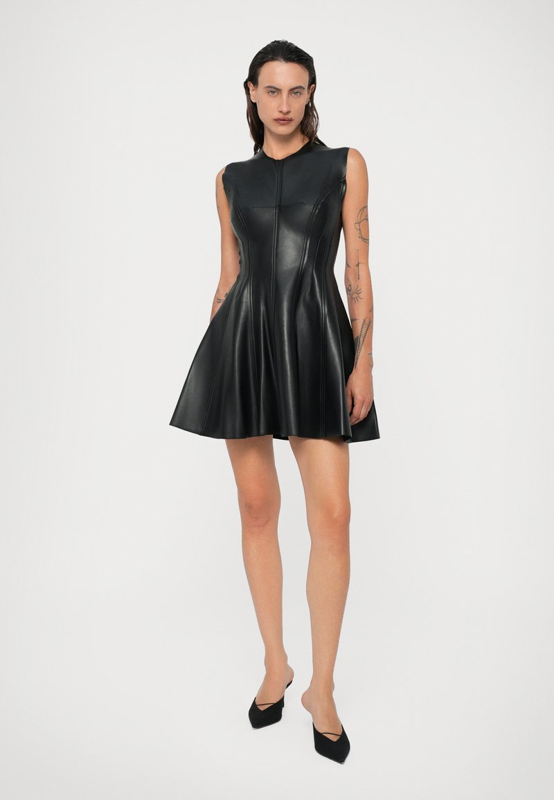 Black sleeveless dress made of leather, featuring a fitted bodice, flared skirt, and vertical seams. Worn with open-toe black shoes.