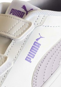 Sneaker bianco con logo PUMA viola. Presenta cinturini in velcro, materiale sintetico liscio e dettagli cuciti per un aspetto testurizzato.